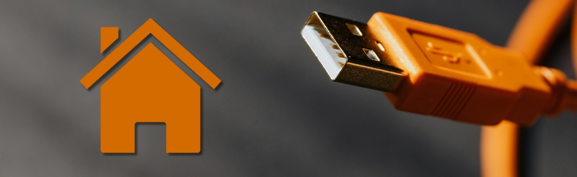 Close-up of an orange USB-A cable beside a home icon, symbolizing Home Assistant server USB add-ons and Z-Wave radio connectivity.